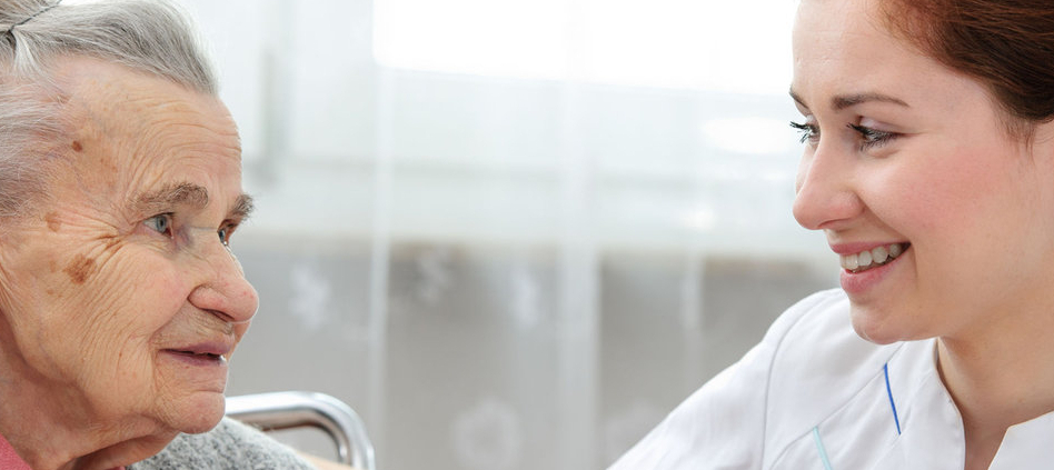 Caregiver helping female resident in a nursing-home-like facility.