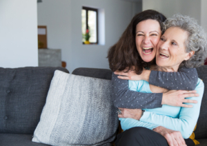 A senior citizen and a younger woman smiling and embracing each other joyfully.